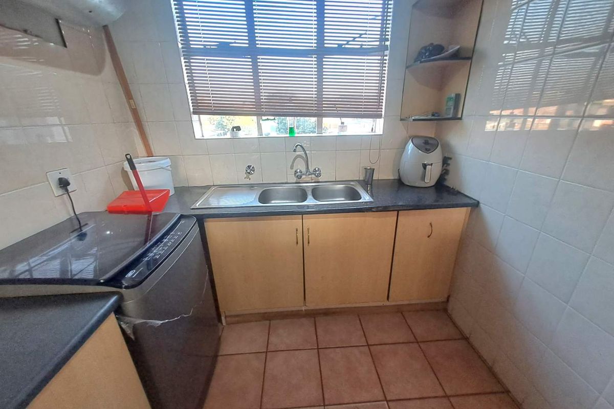 A functional kitchen area featuring laminate cabinetry, a double sink with mixer tap, tiled splashbacks, and tiled flooring.