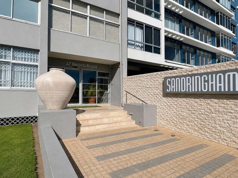 The front entrance of the Sandringham apartment complex, featuring a stone-clad feature wall, paved walkway, and secure building access.