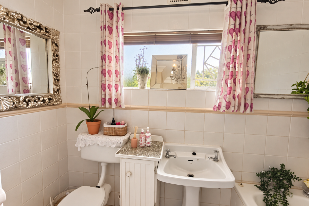 A functional bathroom featuring a pedestal washbasin, toilet, and tiled wall finishes with a window providing natural light.
