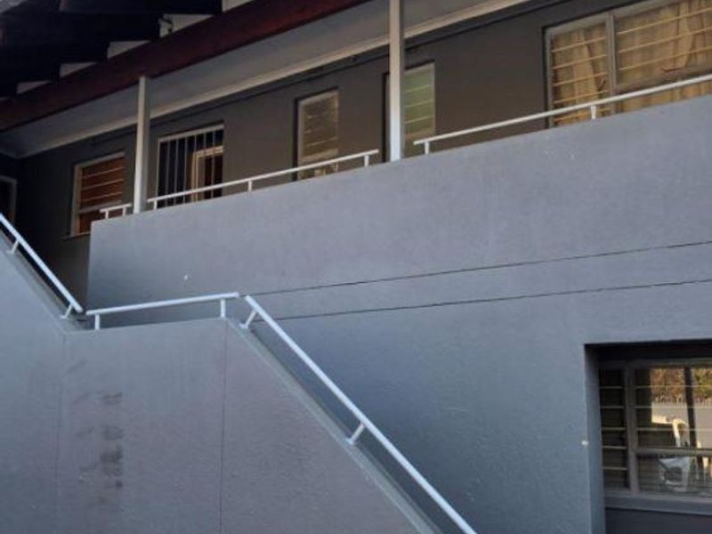Exterior view of an apartment building featuring a staircase, balcony with metal railings, and security bars on the windows.