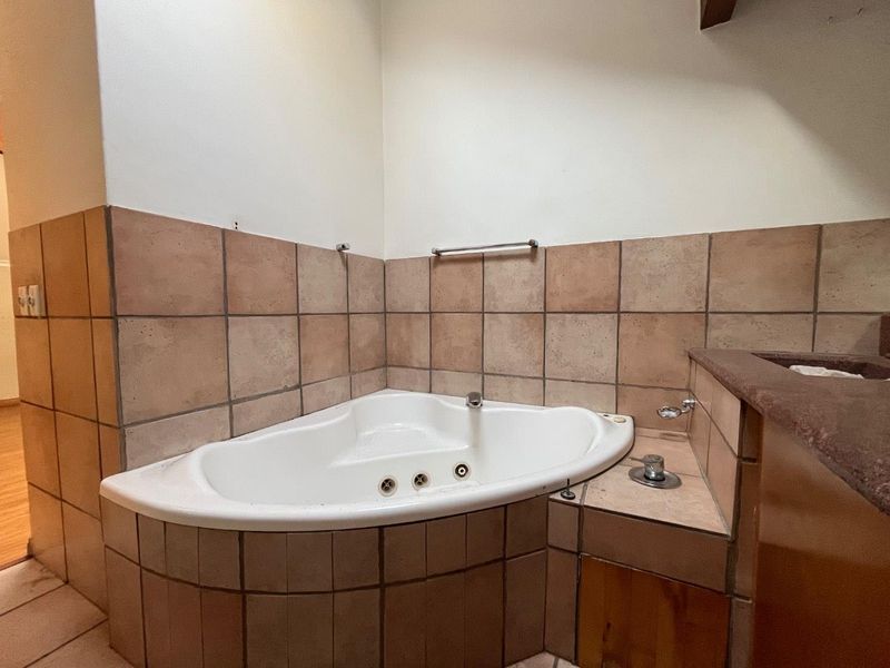A bathroom featuring a corner bathtub with tiled surround and built-in vanity, requiring cosmetic updates to modernize the dated finishes.