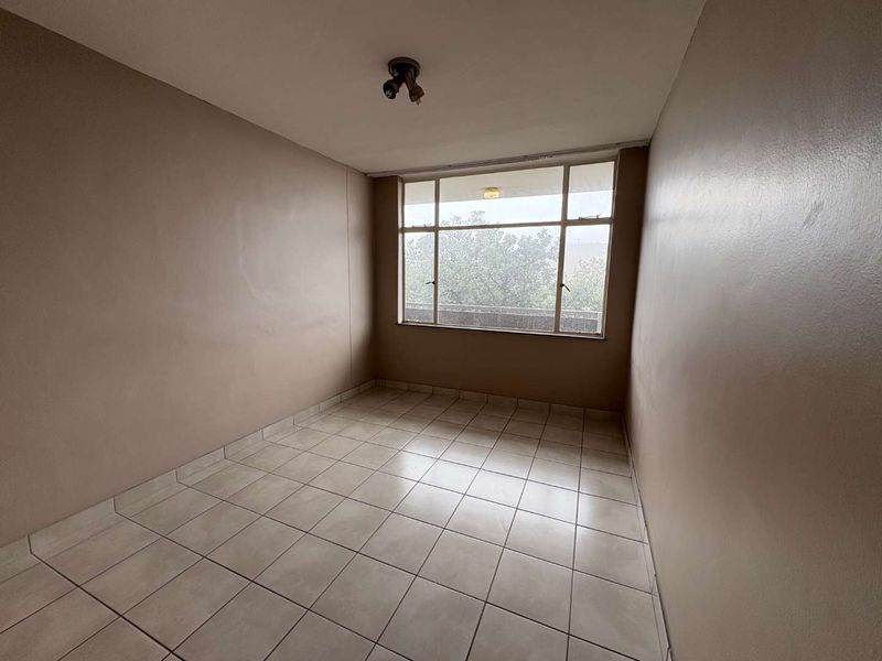 An empty bedroom featuring tiled flooring and a large window providing natural light, ready for personalization.
