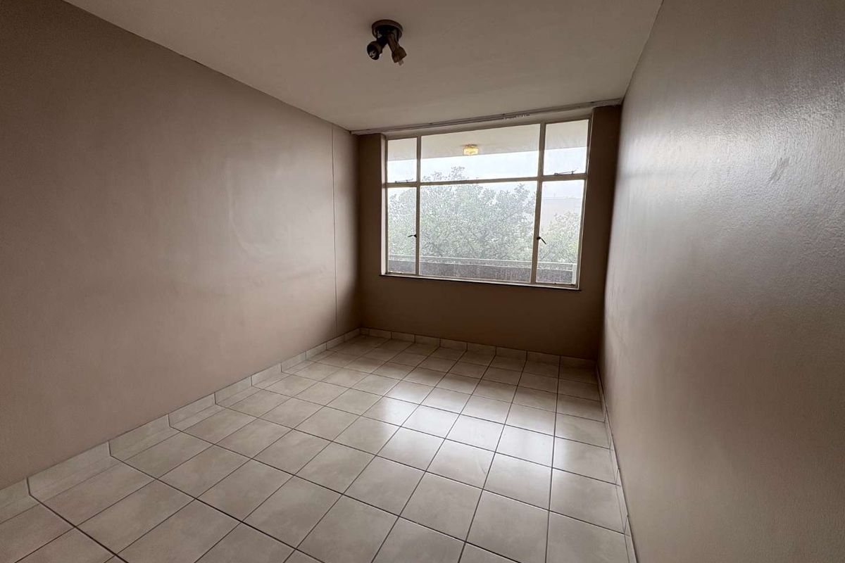 An empty bedroom featuring tiled flooring and a large window providing natural light, ready for personalization.