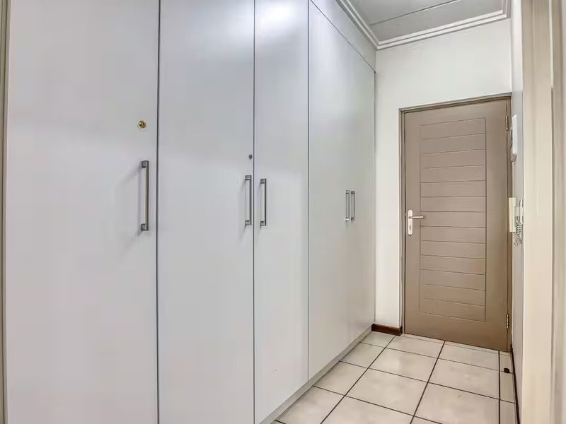 A clean, functional hallway featuring extensive built-in cupboard storage, tiled flooring, and a neutral interior door.