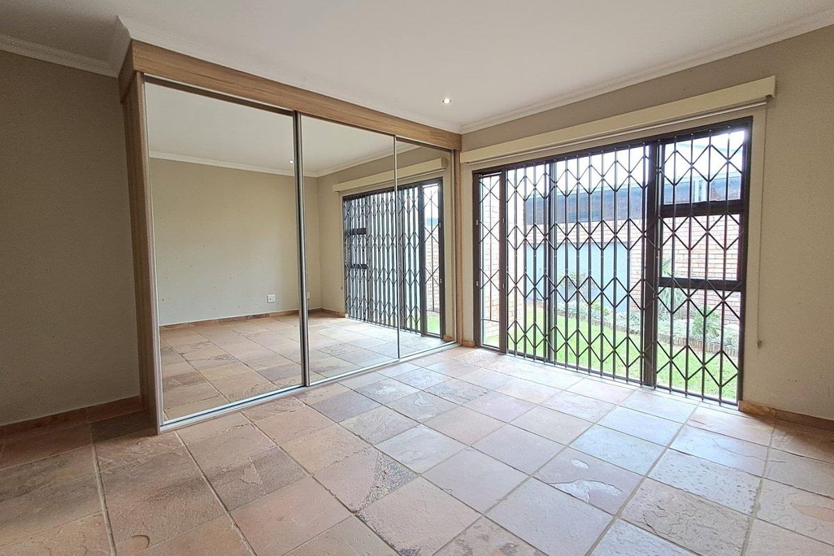 A spacious bedroom featuring large floor tiles, built-in mirrored sliding door cupboards, and security gates leading to the garden area.