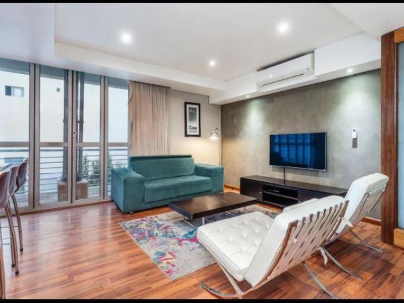 A well-maintained living room featuring hardwood flooring, recessed lighting, a split-system air conditioner, and large sliding glass doors leading to a balcony.