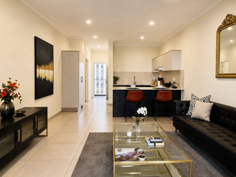 Modern open-plan living area featuring a sleek kitchen with island, tiled flooring, and recessed lighting, seamlessly flowing into a comfortable lounge space.