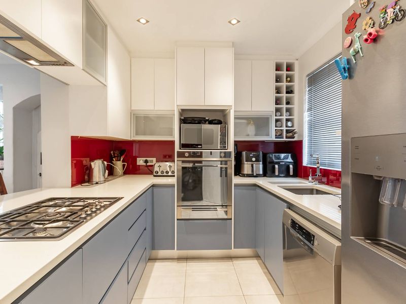Modern U-shaped kitchen featuring two-tone cabinetry, stone countertops, a vibrant red glass splashback, and integrated appliances including a gas hob and built-in oven.