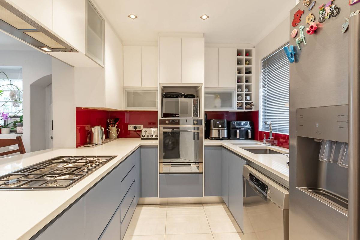 Modern U-shaped kitchen featuring two-tone cabinetry, stone countertops, a vibrant red glass splashback, and integrated appliances including a gas hob and built-in oven.