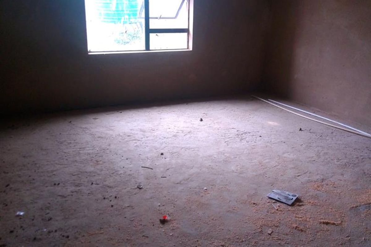 An unfinished bedroom interior featuring raw plaster walls, exposed concrete flooring, and a single window, currently in a shell construction state.
