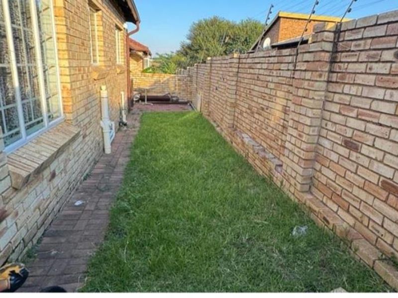 A narrow rear garden area featuring a face brick boundary wall with electric fencing and a paved walkway alongside the townhouse exterior.