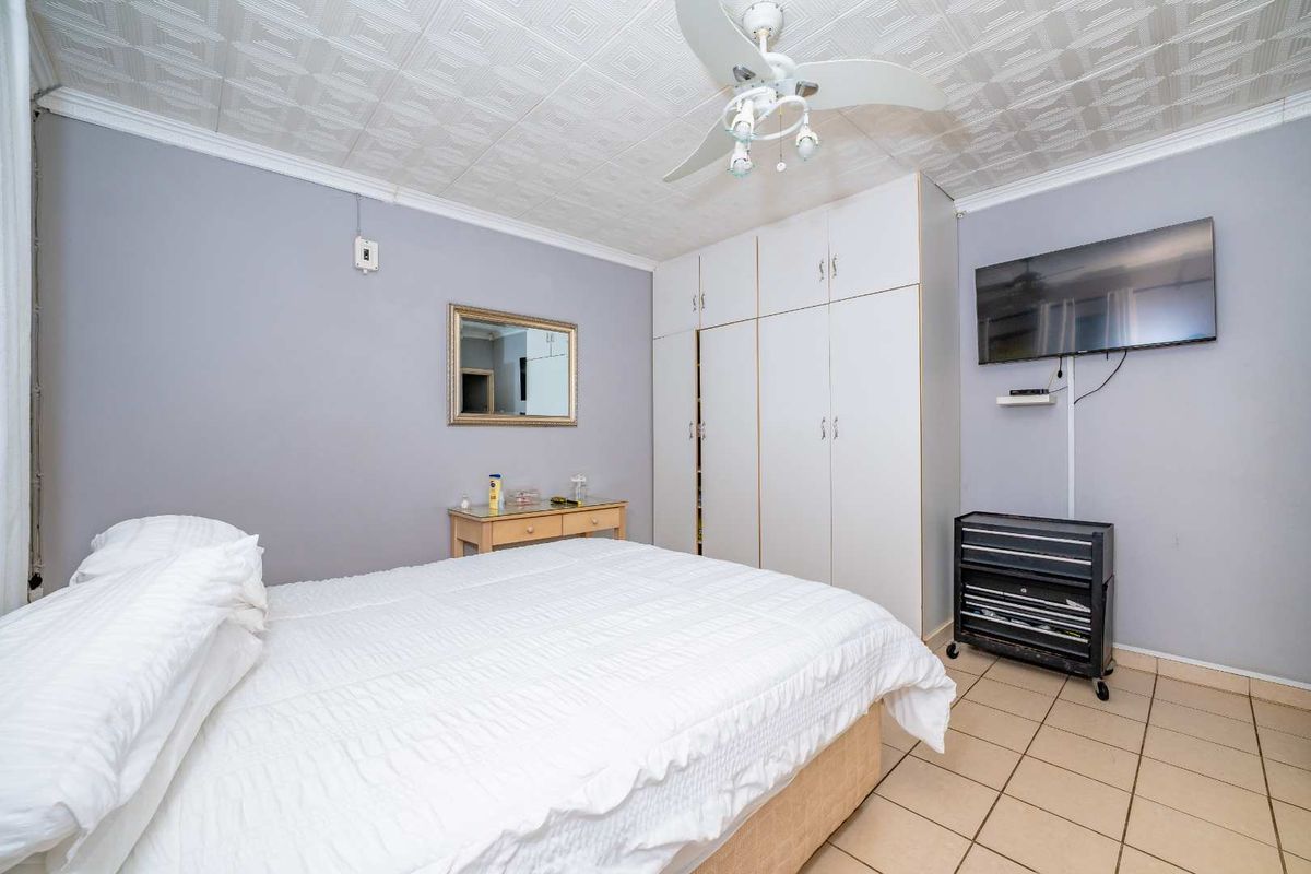 A bedroom featuring built-in cupboards, a ceiling fan, and tiled flooring, providing a functional and well-maintained living space.