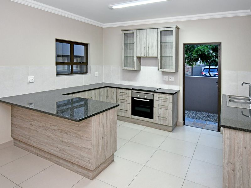 Modern kitchen featuring light wood-grain cabinetry, dark granite countertops, built-in oven and hob, and direct access to an outdoor area.