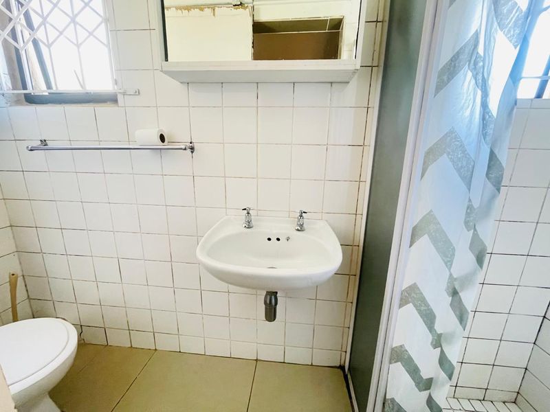 A functional bathroom featuring a wall-mounted basin, tiled surfaces, and a shower enclosure, currently requiring cosmetic updates and maintenance to the wall finishes.