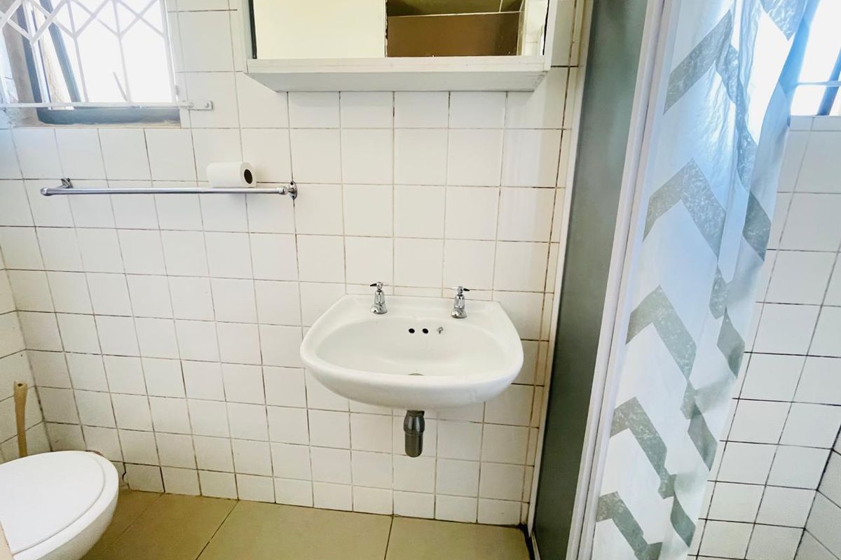A functional bathroom featuring a wall-mounted basin, tiled surfaces, and a shower enclosure, currently requiring cosmetic updates and maintenance to the wall finishes.