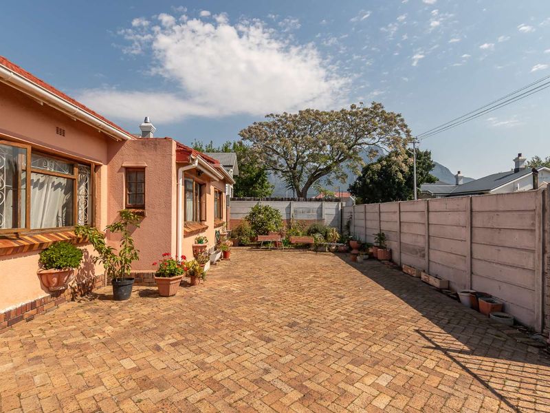 A spacious rear courtyard featuring herringbone brick paving, enclosed by a precast concrete boundary wall, adjacent to the main house structure.
