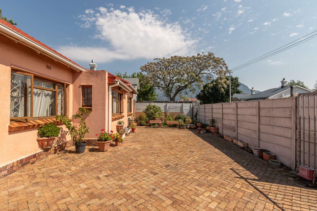 A spacious rear courtyard featuring herringbone brick paving, enclosed by a precast concrete boundary wall, adjacent to the main house structure.