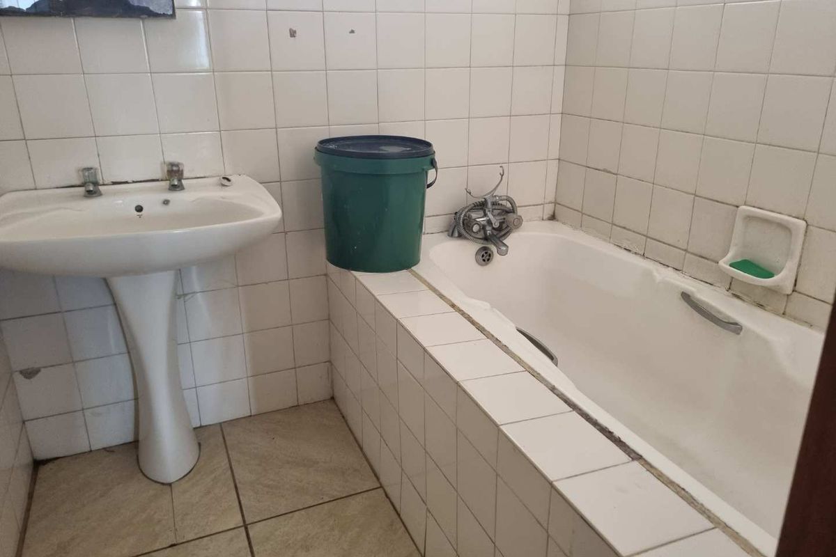 A dated bathroom featuring a pedestal basin and a built-in bathtub with tiled surround, requiring cosmetic updates and maintenance to the tiling and fixtures.