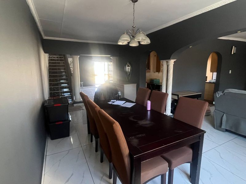 Open plan dining area featuring tiled flooring, decorative columns, and archways leading to adjacent living spaces and a staircase.