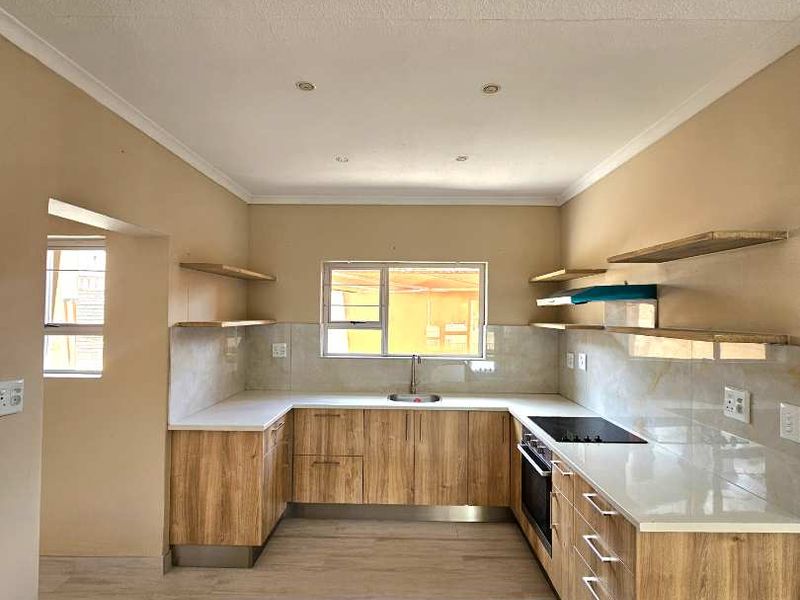 Modern U-shaped kitchen featuring wood-finish cabinetry, stone countertops, built-in oven, electric hob, and floating shelving in a clean, open-plan layout.