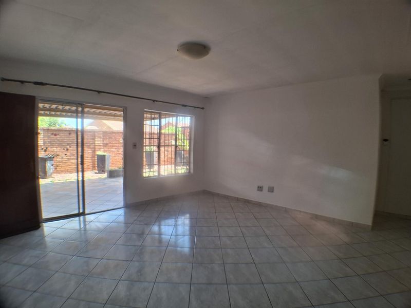 An empty, open-plan living area featuring neutral tiled flooring, large windows with security bars, and a sliding door providing access to the rear patio.