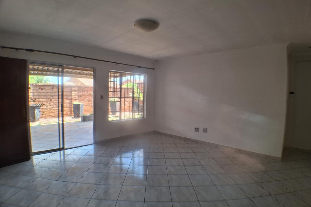 An empty, open-plan living area featuring neutral tiled flooring, large windows with security bars, and a sliding door providing access to the rear patio.