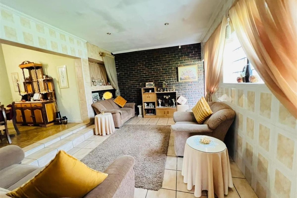 A spacious living area featuring a dark brick feature wall, tiled flooring, and a raised transition area leading to an adjacent room.