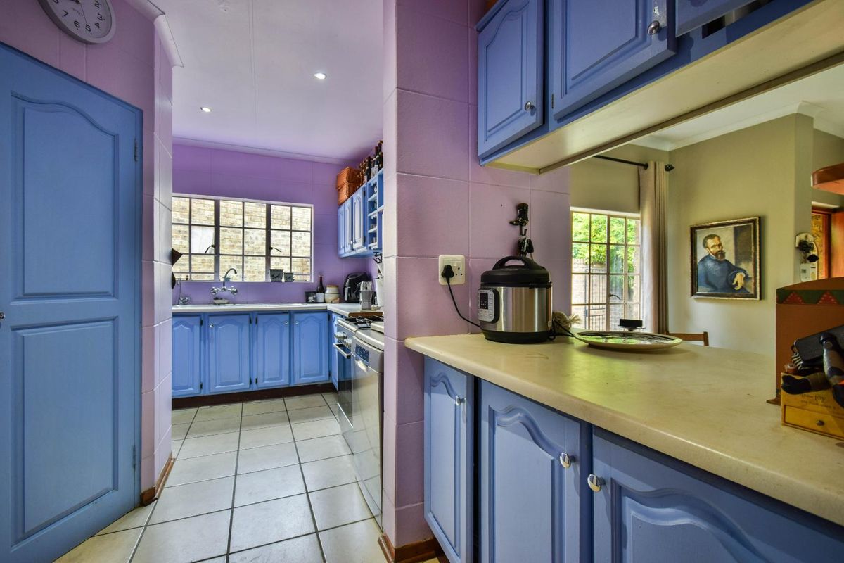 A functional kitchen featuring blue cabinetry, tiled flooring, and a breakfast bar pass-through, offering a practical layout with ample storage space.