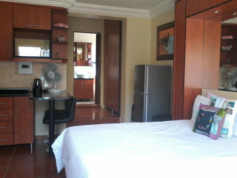 Open-plan studio apartment featuring a compact kitchenette with built-in cabinetry, tiled flooring, and an integrated bedroom area with a built-in headboard.