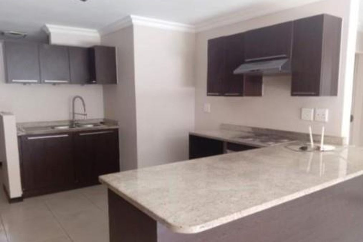 Modern kitchen featuring dark wood cabinetry, stone countertops, a breakfast bar, and integrated extractor fan, offering a clean and functional workspace.
