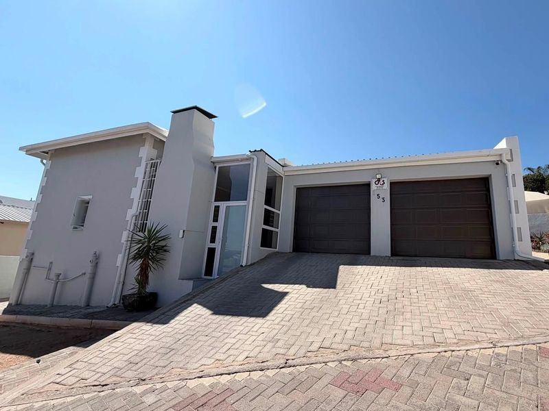 Front elevation of a modern house featuring a double garage, paved driveway, and a prominent chimney stack.