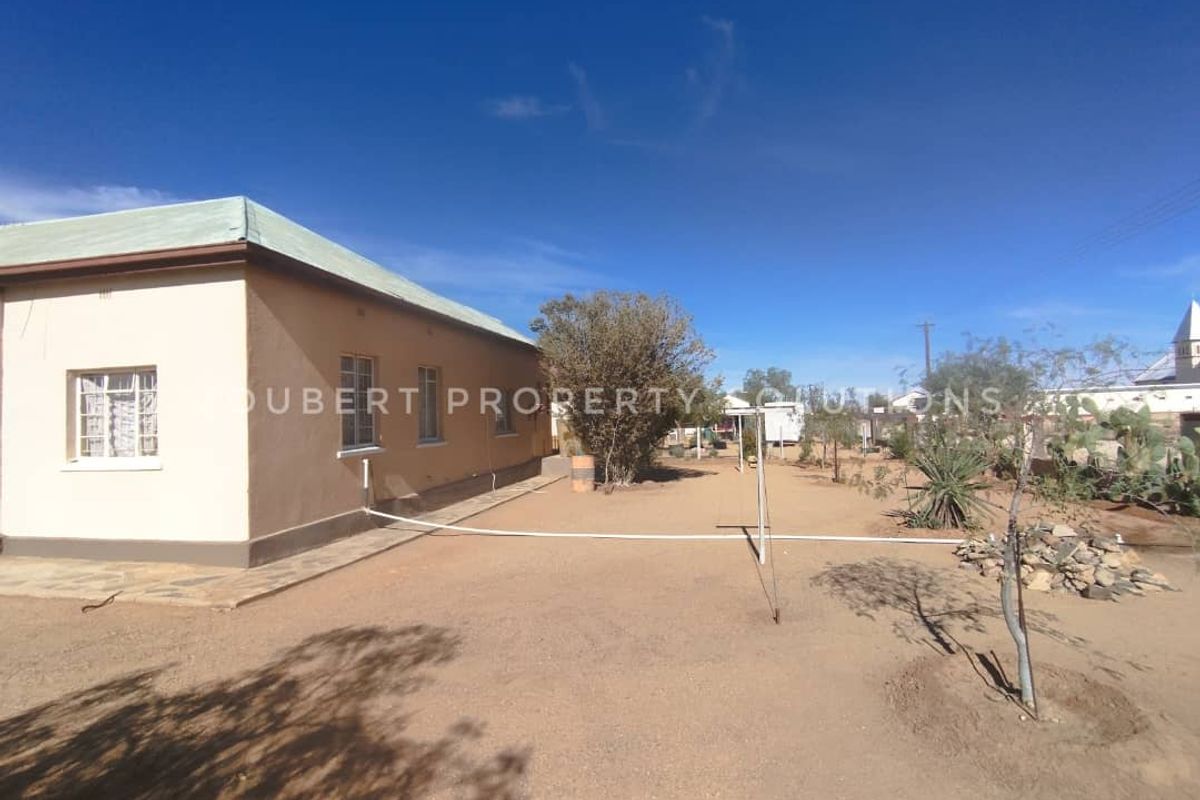 Exterior view of the property showing the side facade, basic window frames, and a large, unlandscaped yard area.