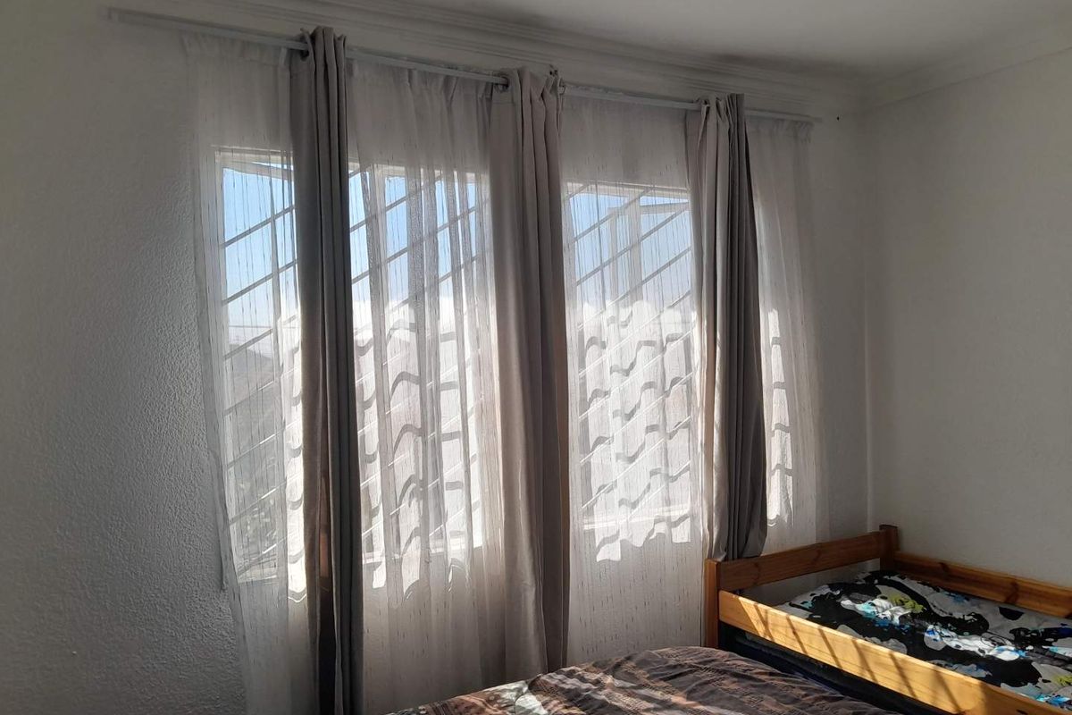 A bedroom featuring large windows with security bars and installed curtain rods, providing natural light.