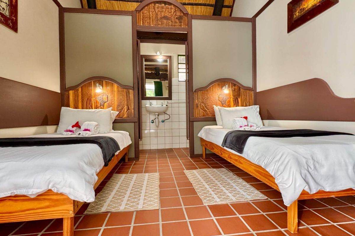 A twin bedroom featuring a thatched roof, tiled flooring, and an integrated en-suite bathroom area with a wall-mounted basin.