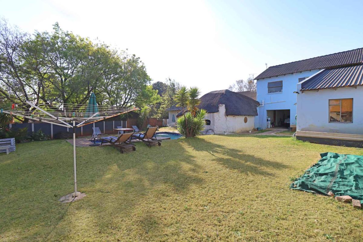 Rear garden view featuring a swimming pool, paved patio, and a secondary thatched roof structure adjacent to the main house.