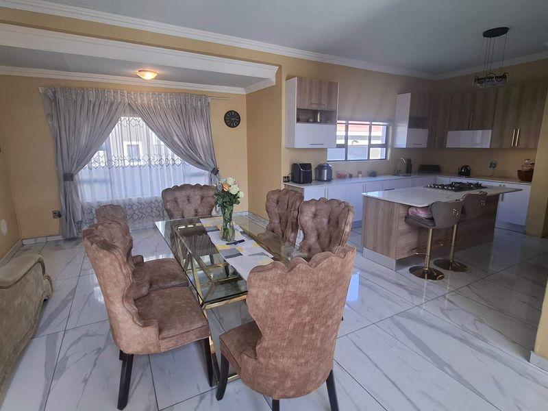 Spacious open-plan living and dining area featuring a modern kitchen with a central island, gas hob, and polished marble-look floor tiles.