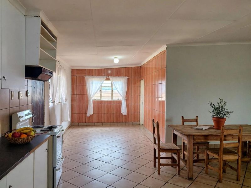 Open-plan kitchen and dining area featuring tiled flooring, dated wall tiling, and functional built-in cabinetry.