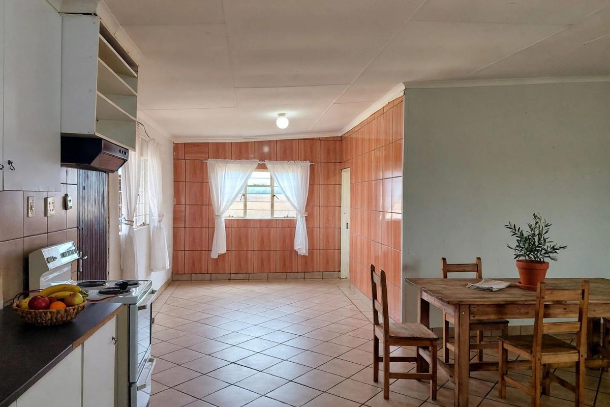 Open-plan kitchen and dining area featuring tiled flooring, dated wall tiling, and functional built-in cabinetry.
