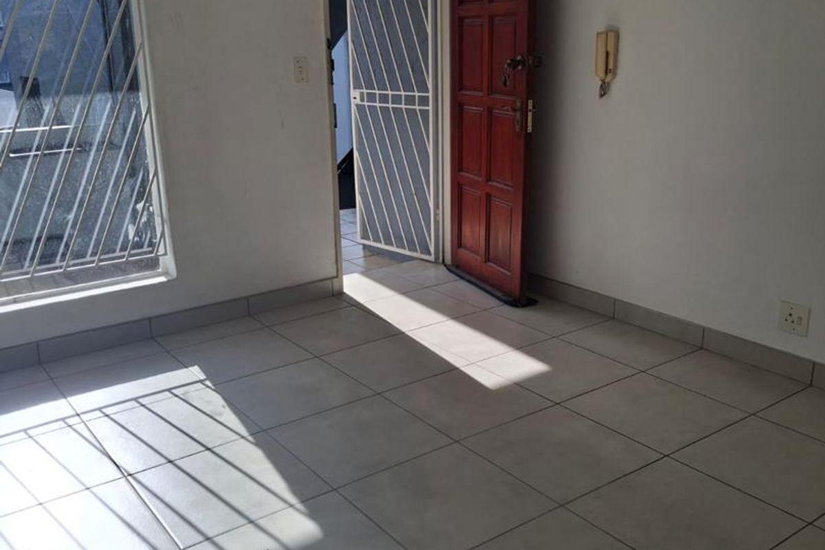 An empty living area featuring tiled flooring, a security gate at the entrance, and a window fitted with security bars.