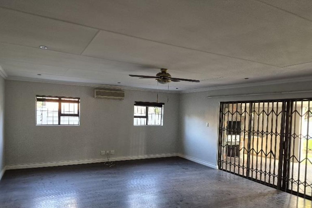 Spacious living area featuring a ceiling fan, wall-mounted air conditioning unit, and large sliding doors with security gates leading to the exterior.