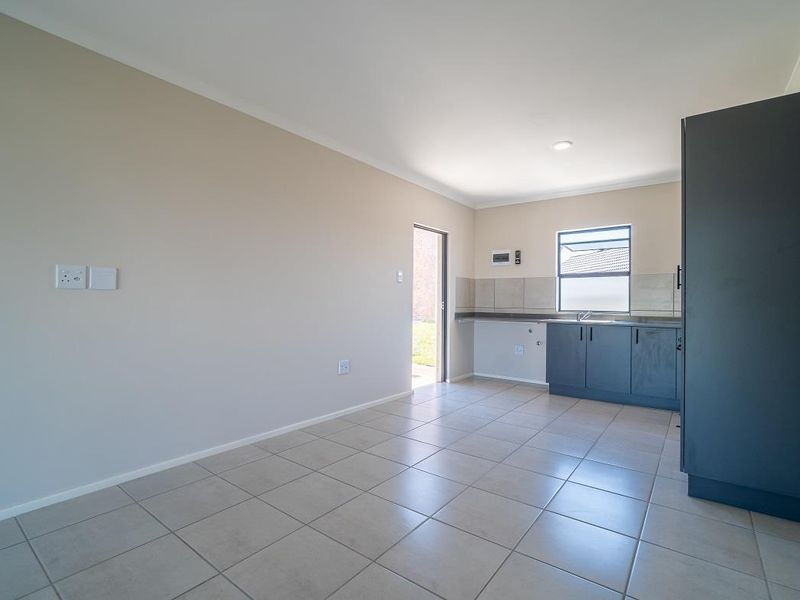 A clean, modern kitchen area featuring dark cabinetry, tiled flooring, and a stainless steel sink, presented in an empty, well-maintained space.