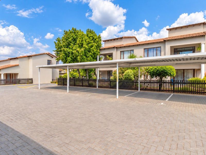 A well-maintained apartment complex exterior featuring paved parking bays with covered carports and landscaped surroundings.