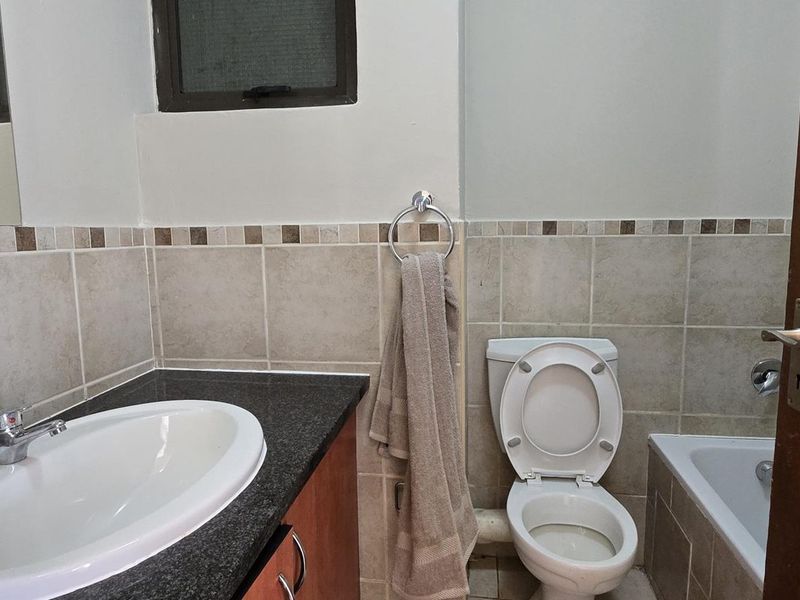 A functional bathroom featuring a vanity with granite countertop, drop-in basin, toilet, and a bathtub with tiled surround.