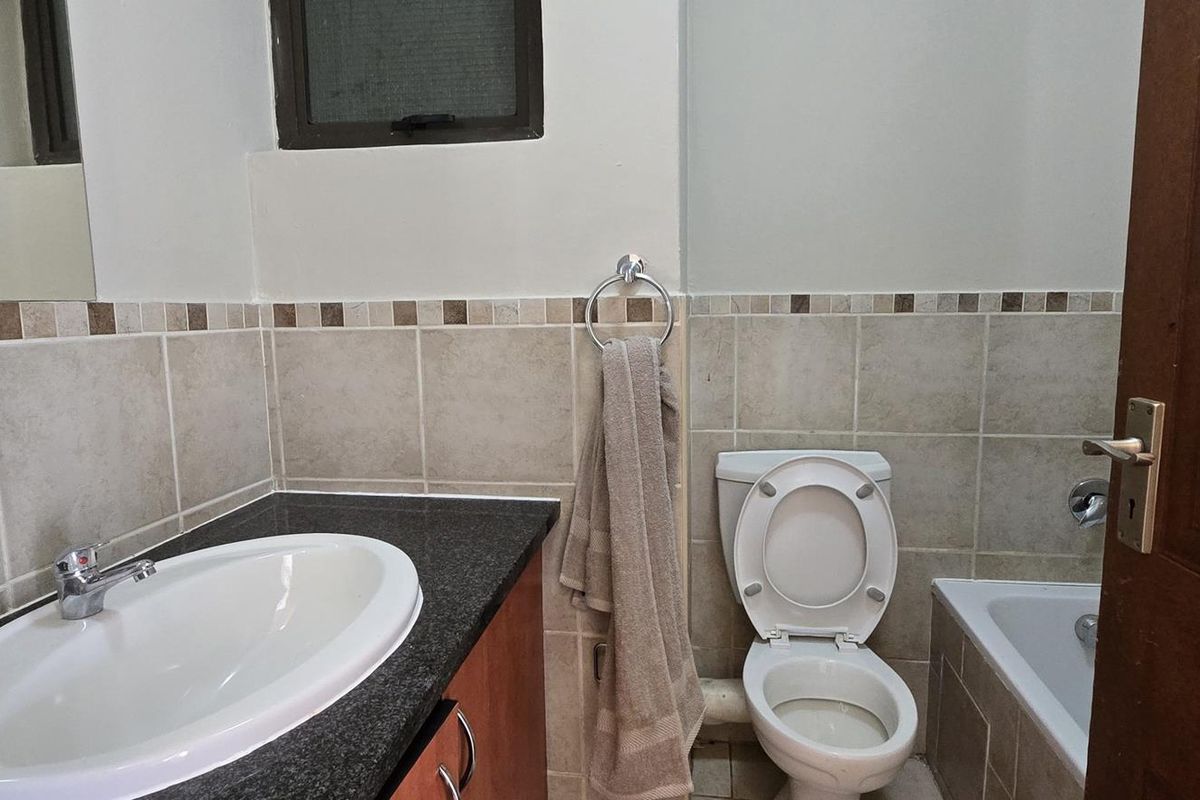A functional bathroom featuring a vanity with granite countertop, drop-in basin, toilet, and a bathtub with tiled surround.