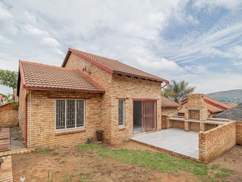 Rear view of a face brick townhouse featuring a tiled patio with a built-in brick braai and a small garden area.
