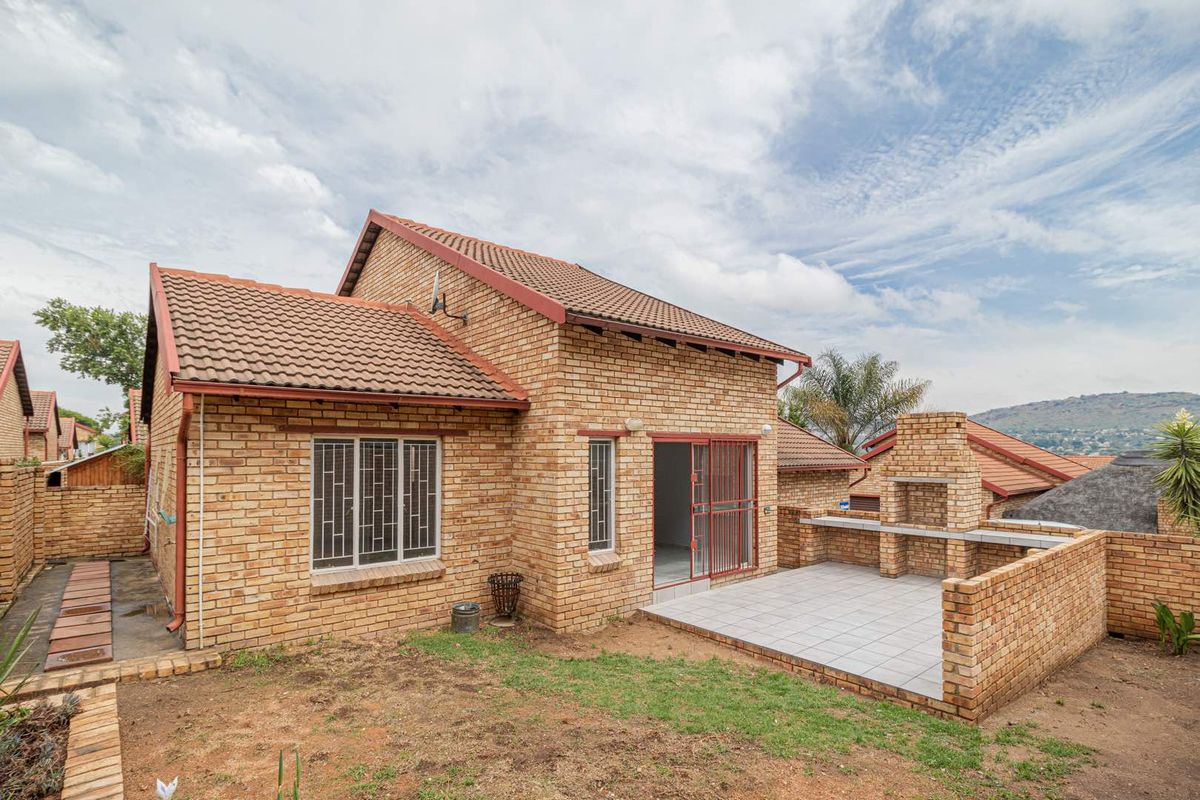 Rear view of a face brick townhouse featuring a tiled patio with a built-in brick braai and a small garden area.