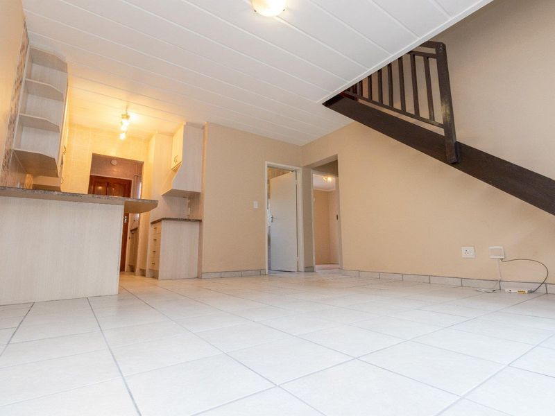 Open plan living area featuring tiled floors, a compact kitchen with stone countertops, and a staircase leading to the upper level.