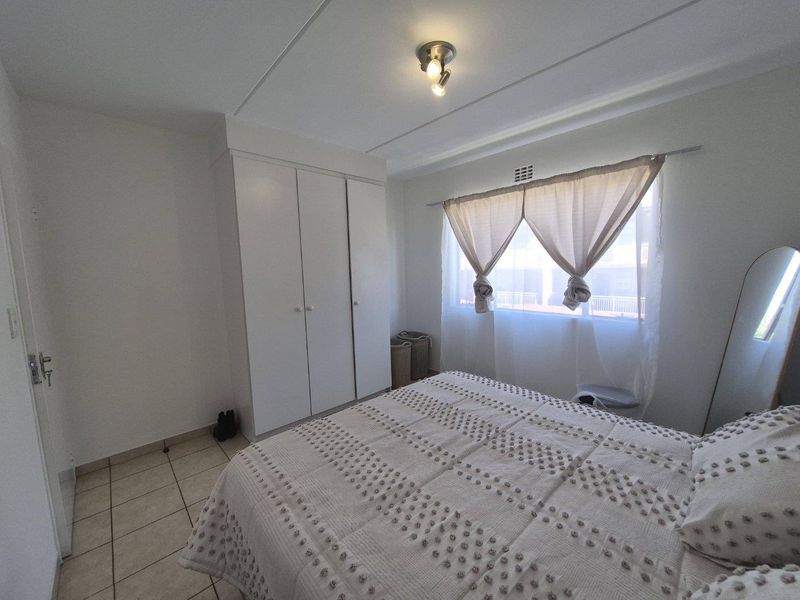 A functional bedroom featuring built-in cupboards, tiled flooring, and natural light through a window with curtaining.