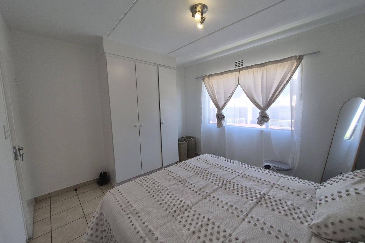 A functional bedroom featuring built-in cupboards, tiled flooring, and natural light through a window with curtaining.