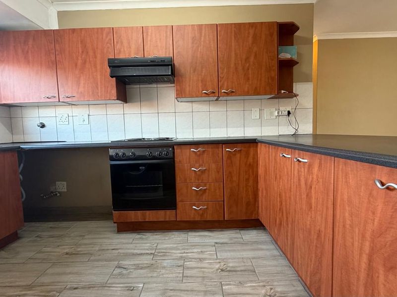 A dated kitchen featuring wood-look laminate cabinetry, dark countertops, and tiled flooring, requiring minor repairs and cosmetic updates to modernize the space.